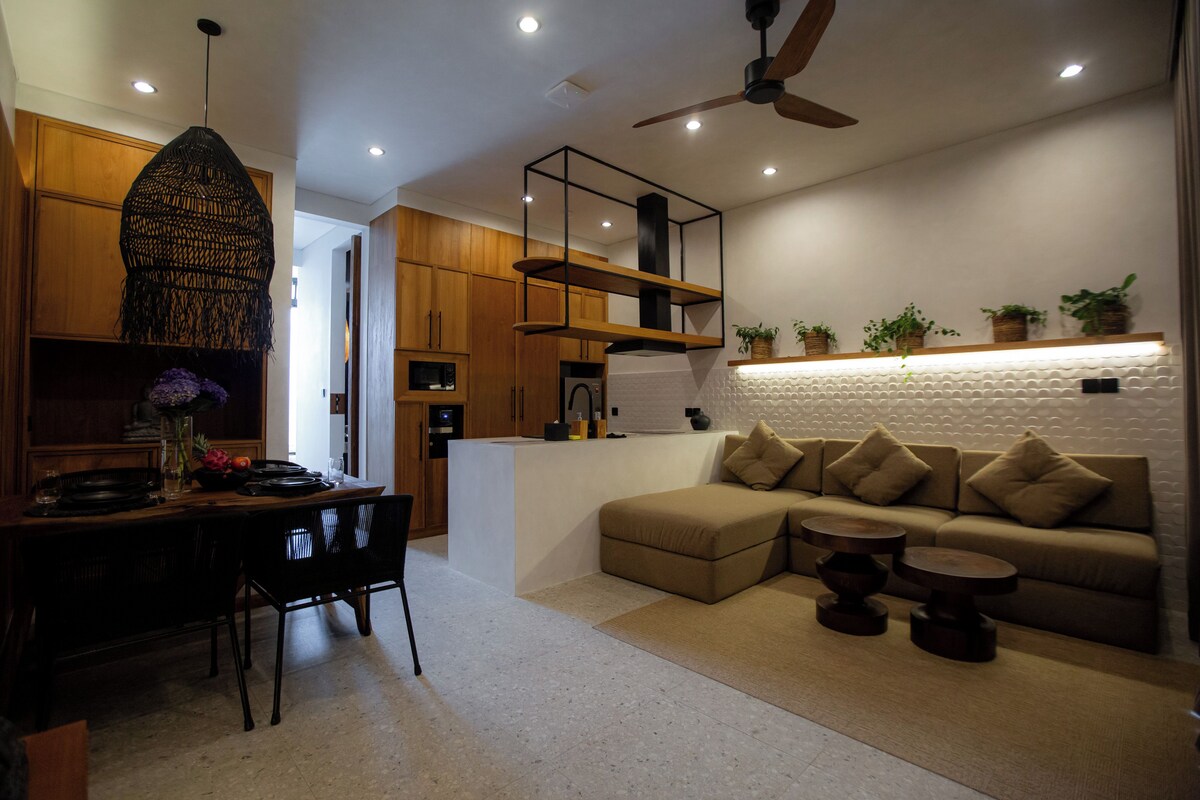 Ein modernes Wohnzimmer mit Sofa, Couchtisch, Essbereich mit Stühlen, Holzschränken und Deckenventilator.
