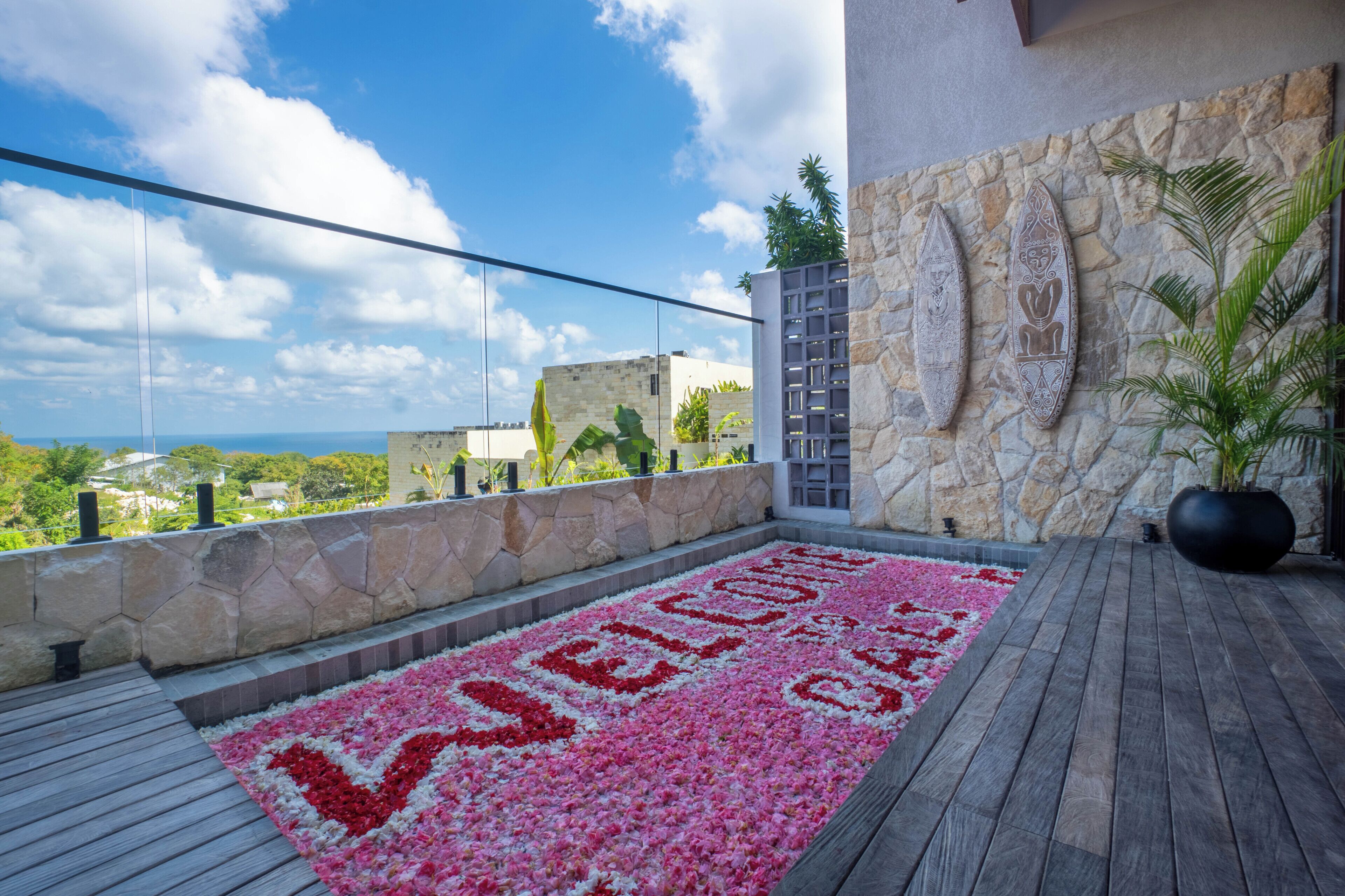 Un balcón con pared de piedra, un adorno mural y un manto floral que deletrea 'WELCOME'.