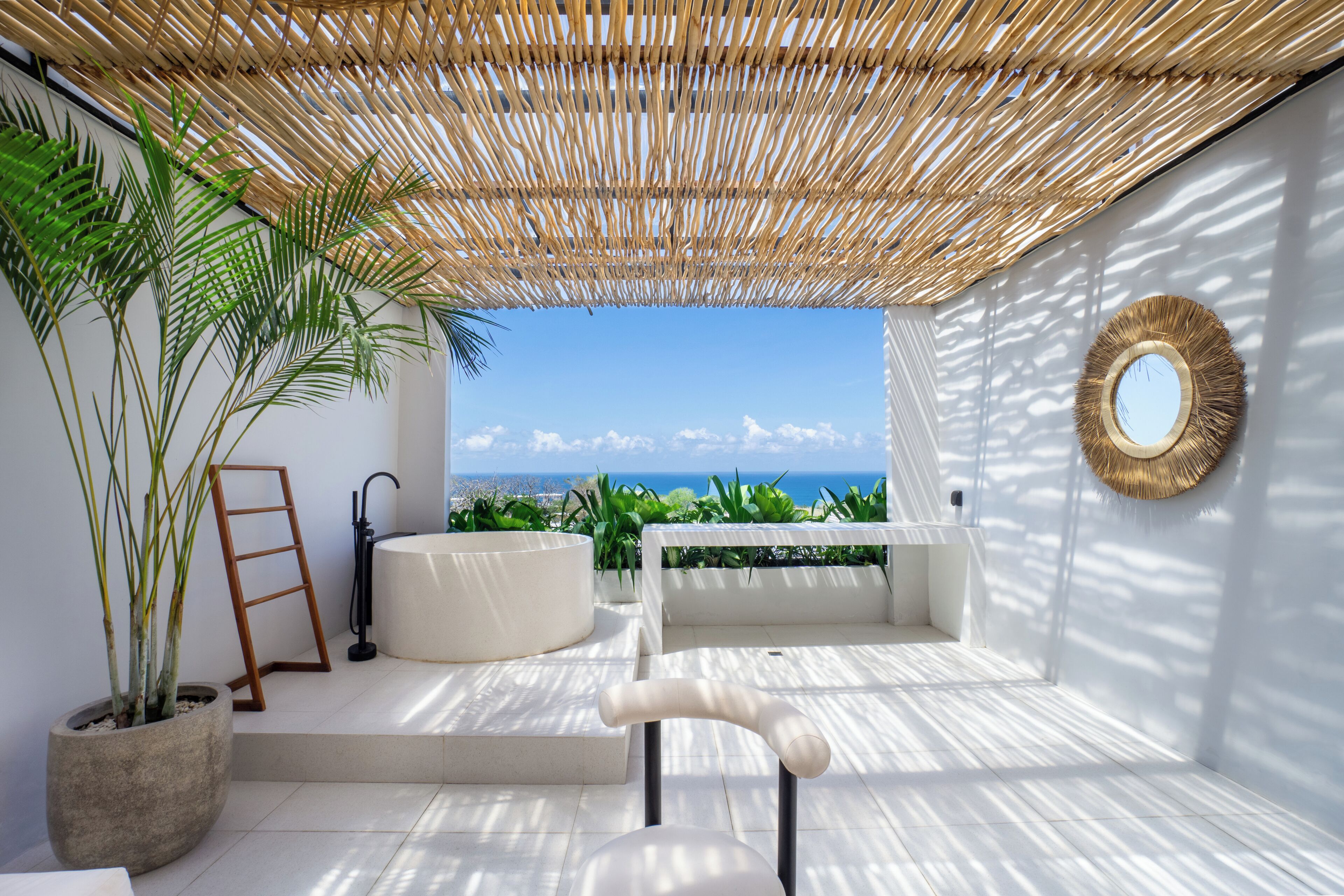 A modern outdoor seating area with a view of the ocean, a large potted plant, and a mirror on the wall.