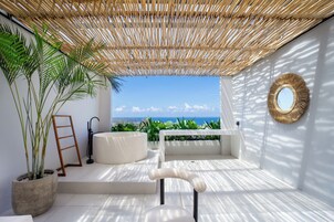 A modern outdoor seating area with a view of the ocean, a large potted plant, and a mirror on the wall.