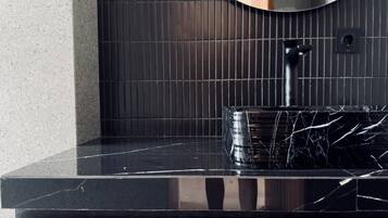 A bathroom with a black marble sink, a round mirror, and a tiled wall.