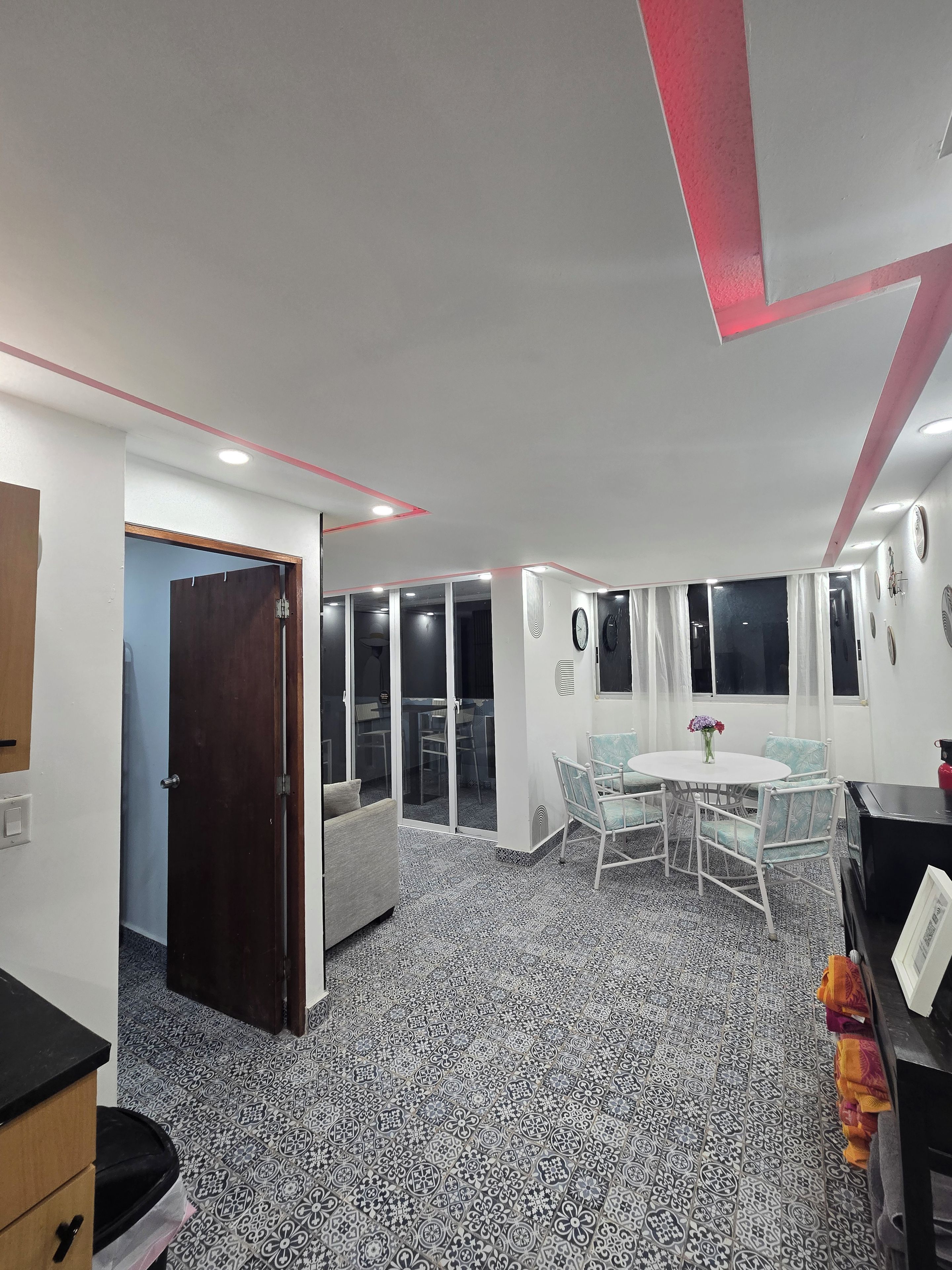 Ein modernes Zimmer mit einem gemusterten Boden, einem Essbereich mit Stühlen und einem Tisch sowie einer Tür zu einem weiteren Raum.