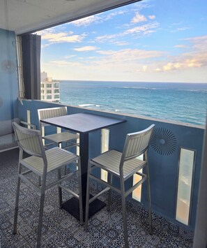 A balcony with a table and chairs, overlooking the sea.