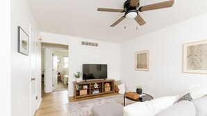 A living room with a grey sofa, a wooden entertainment unit, a ceiling fan, and a flat-screen TV.
