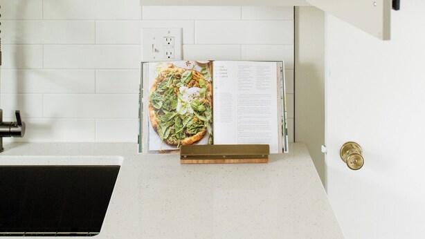 A kitchen with white cabinets, a wooden shelf with dishes, a kettle, and a pizza menu on the counter.