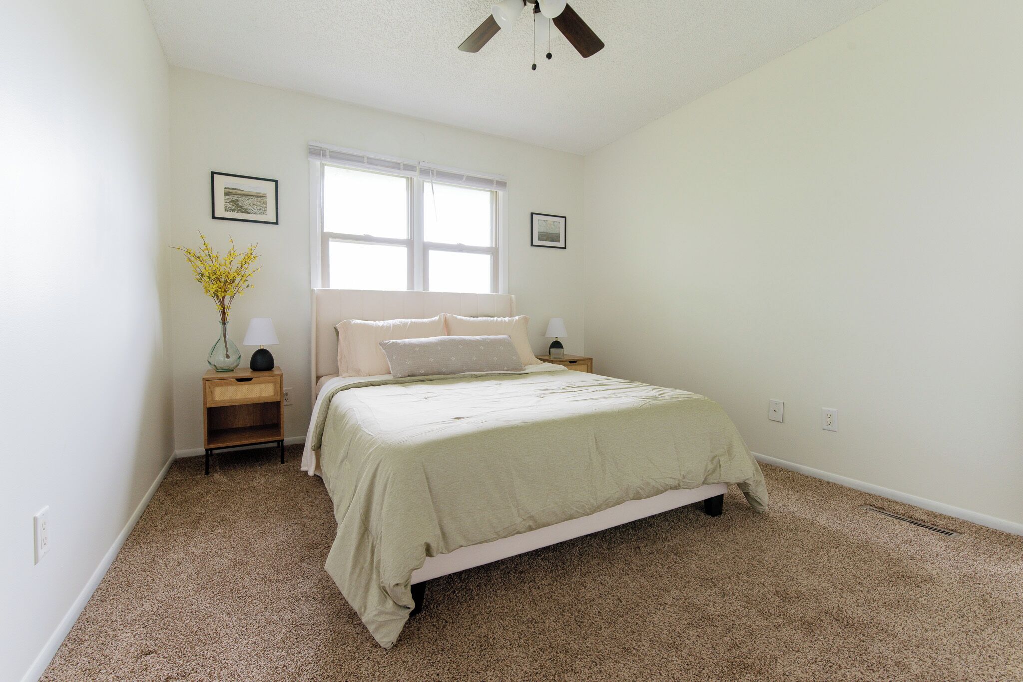 Une chambre à coucher avec un lit, deux tables de chevet, une fenêtre et un ventilateur de plafond.