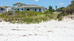 Een pand aan het strand met een huis, zandstrand en weelderige begroeiing.