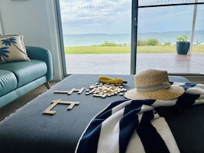 Une pièce avec vue sur la mer, un canapé, une table avec des lettres de Scrabble, un chapeau et une couverture.