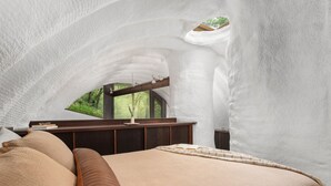 Une chambre à coucher avec un plafond en arc, un lit, un bureau et une fenêtre donnant sur une forêt.