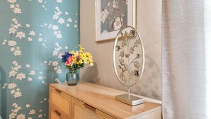 Eine Holzkommode mit einer Vase bunter Blumen, einem gerahmten Blumenbild und einem dekorativen Spiegel darauf.