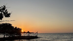 A sunset view over a calm sea with a beach and trees in the foreground. - Hotel Colombia del Golfo (Tolú)