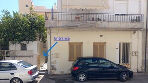 A building with an entrance marked by a blue arrow. There are two cars parked in front. - Comfy studio near city center (Heraklion)