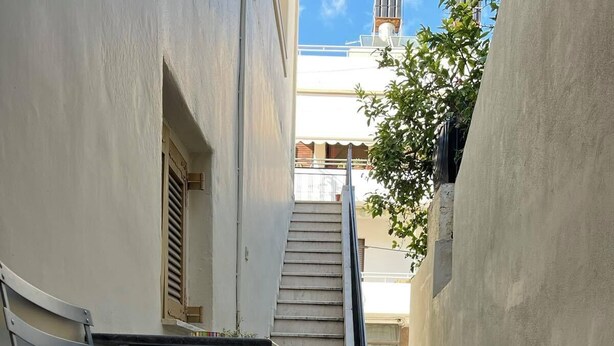 A narrow outdoor corridor with a metal bench, a staircase, and a vehicle parked in the background. - Comfy studio near city center (Heraklion)