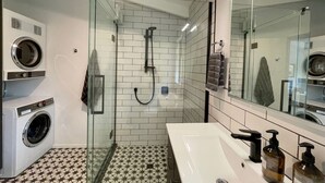 Een moderne badkamer met een douchecabine van glas, een witte wastafel met spiegel en een wasmachine.