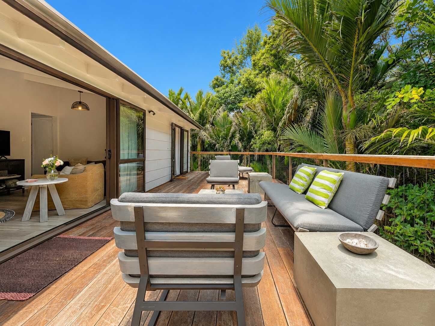 Un espacio exterior moderno con terraza de madera, un sofá con cojines, una mesa de comedor y una silla.
