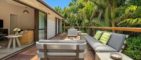 Un espacio exterior moderno con terraza de madera, un sofá con cojines, una mesa de comedor y una silla.