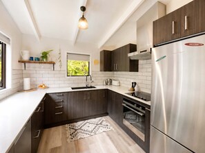 Een moderne keuken met donkere kastjes, witte aanrechtbladen, een roestvrijstalen koelkast en een raam met uitzicht op groen.