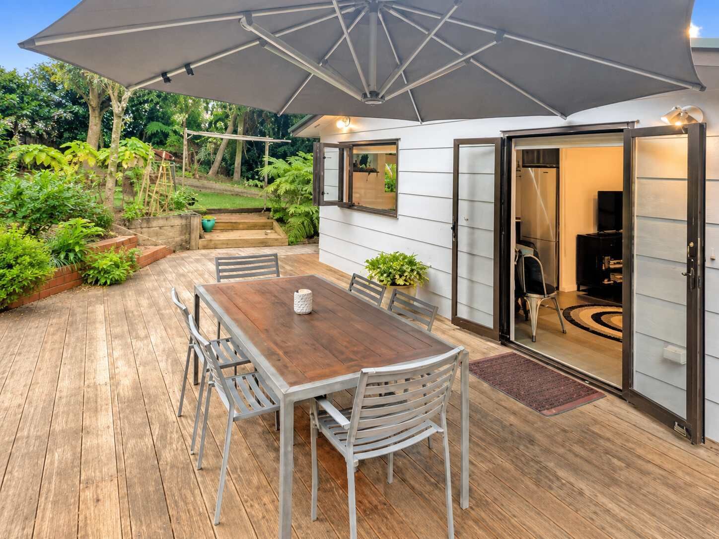 A patio with a wooden table and chairs, a large umbrella, and a sliding glass door leading to an interior space.