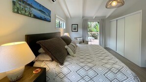 Een slaapkamer met een bed, nachtkastje, lamp, airconditioner, raam en uitzicht op de omgeving.
