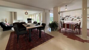 A spacious living area with a dining table, sofas, and a kitchen in the background. - Lou Quillé - UZEIN - Gîte (UZEIN)