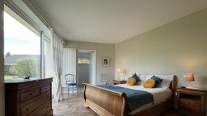 A bedroom with a wooden bed, a dresser, a chair, and a nightstand with lamps. - Lou Quillé - UZEIN - Gîte (UZEIN)