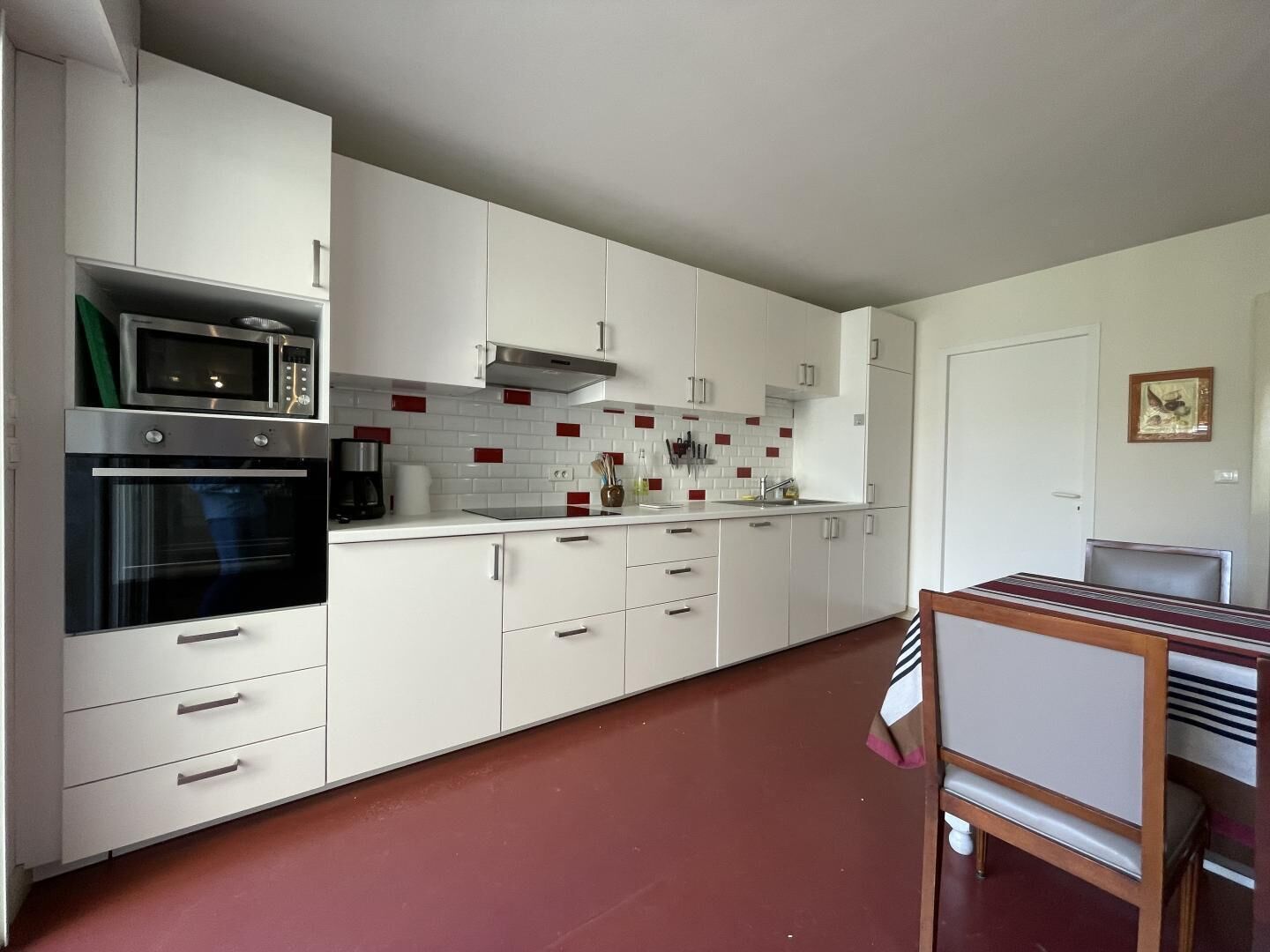 A modern kitchen with white cabinets, a microwave, oven, and a red-tiled backsplash.