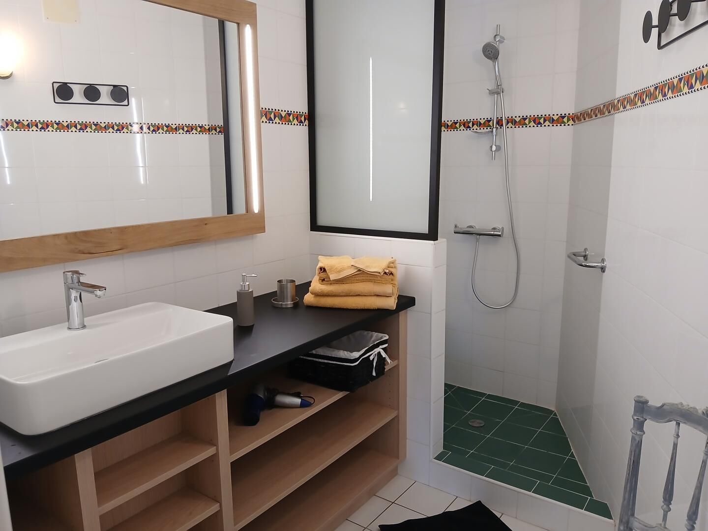 Un baño con lavamanos, espejo, toallero, ducha y estante con artículos de aseo.