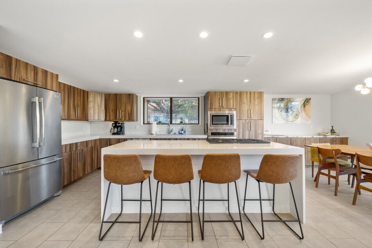 Una cocina moderna con una isla central, taburetes de bar y un comedor con sillas de madera.