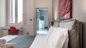 A hotel room with a bed, a desk, a red chair, and a painting on the wall.