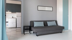 A modern room with a grey sofa, a small side table, and a kitchen area visible through an open door.