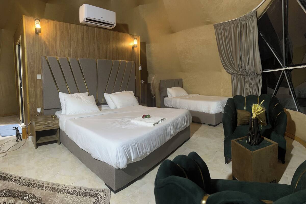 A hotel room with two beds, a wooden headboard, a small table with a vase, and a curtain.