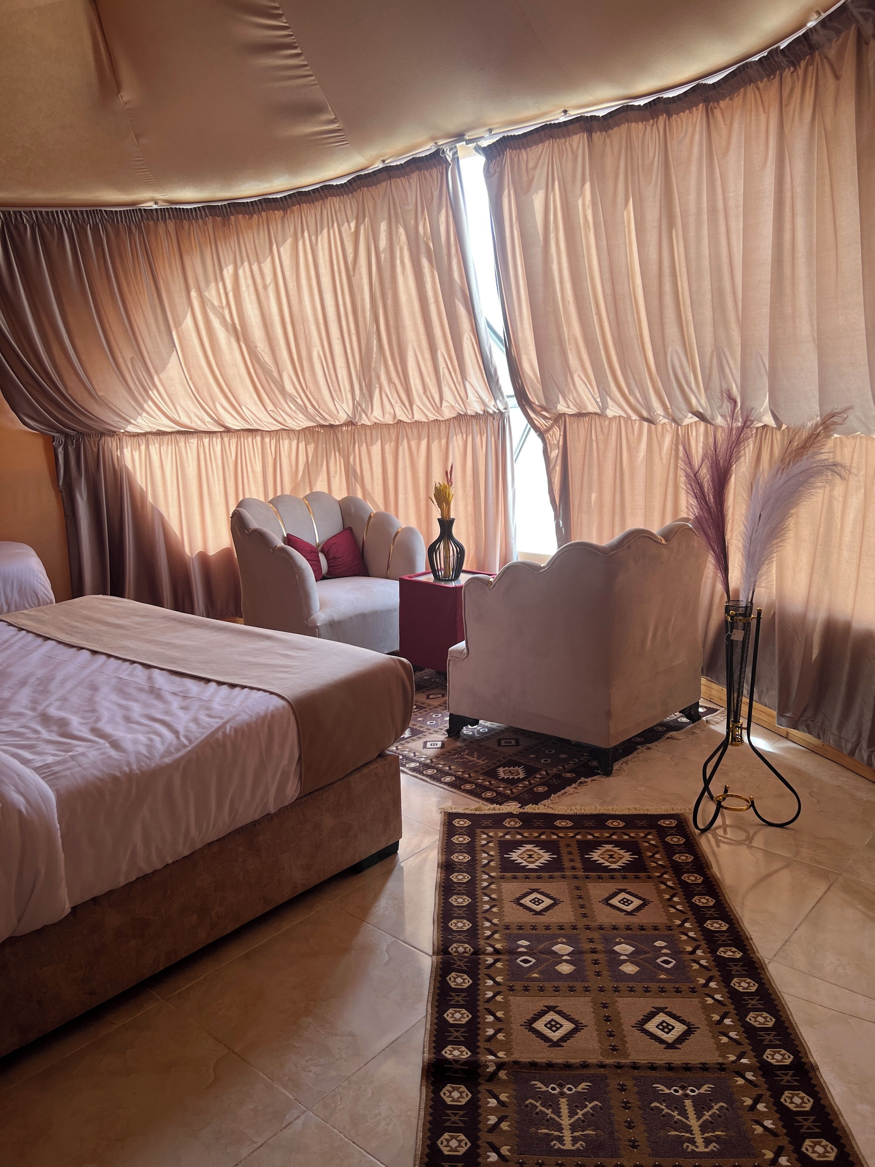 A room with two beds, a sofa, a small table with a vase, and a decorative plant.