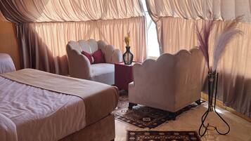 A room with two beds, a sofa, a small table with a vase, and a decorative plant.