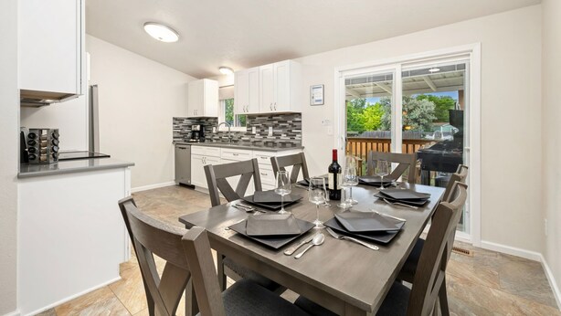 Une cuisine moderne avec des meubles blancs, un plan de travail noir et un coin repas doté d’une table en bois, mise pour six personnes.