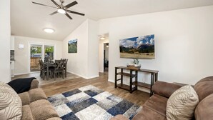 Un salon doté d’un ventilateur de plafond, un coin repas avec une table et des chaises, et un grand tableau accroché au mur.