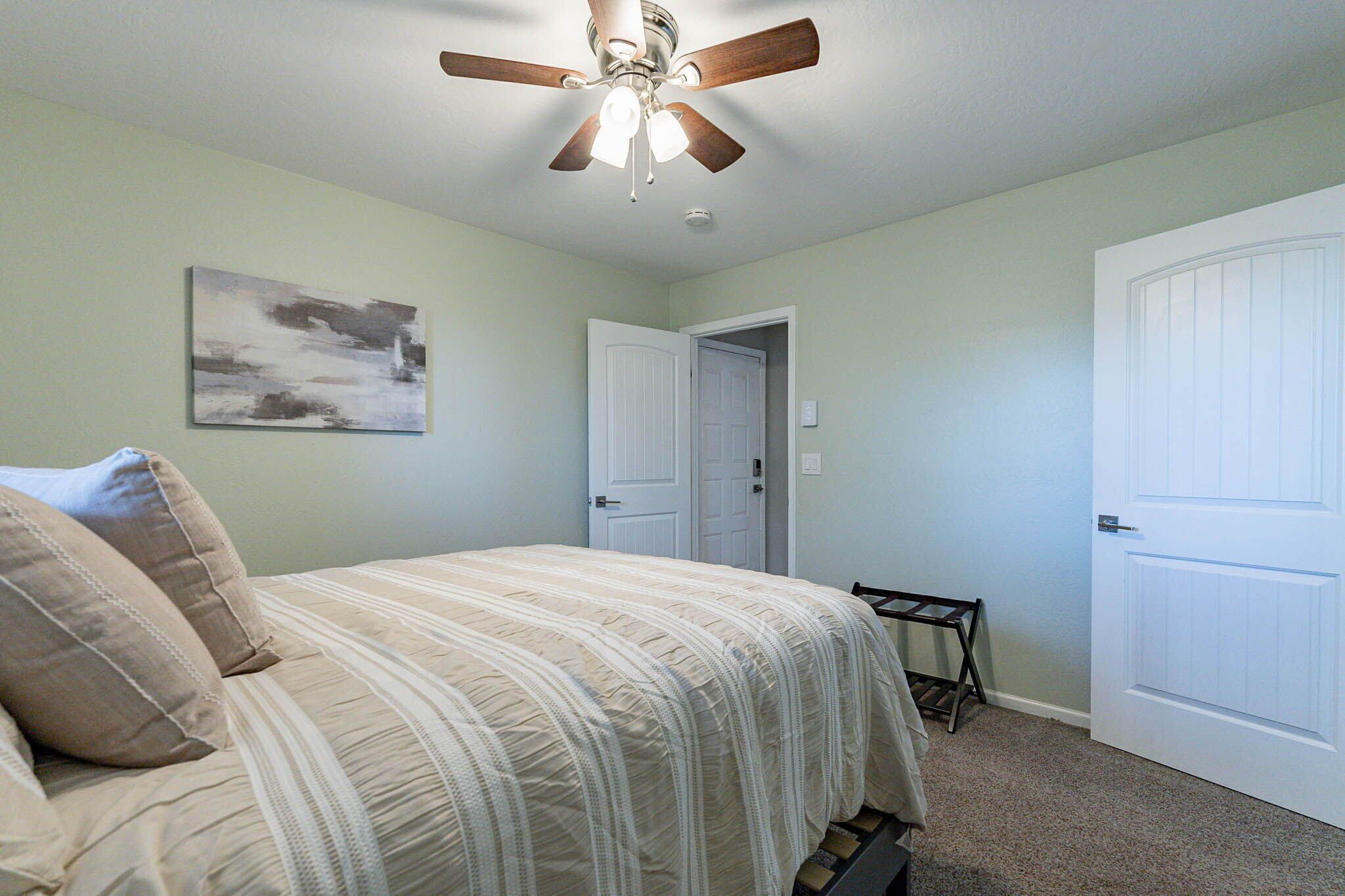 A bedroom with a bed, a ceiling fan, a door, and a small table.