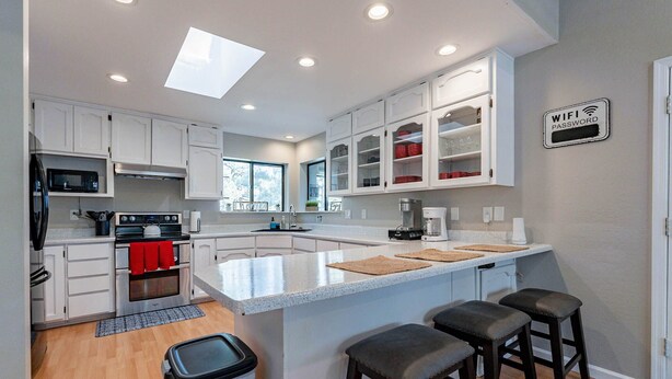 Una cocina moderna con armarios blancos, una isla central con taburetes, microondas, estufa y un cubo de basura.