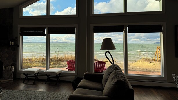 A spacious living room with large windows overlooking the ocean, a ceiling fan, and a red chair by the window.
