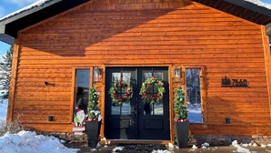 A wooden cabin with a black front door, two wreaths, and a number "7660" on the right side.