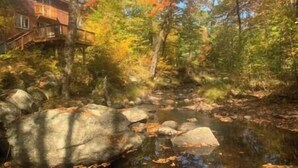 A river with rocks and trees, a wooden bridge, and a building with a balcony.
