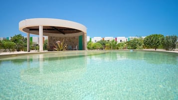 A clear pool with a covered pavilion and a view of buildings in the background.