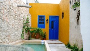 A narrow courtyard with a blue door, a small pool, and potted plants. - Casa Tiago - Downtown & Romance by LAHOS (Mérida)