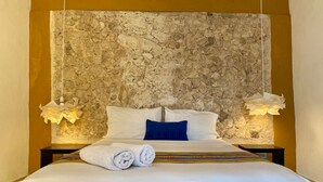 A hotel room with a stone-textured headboard, a neatly made bed with white linens, and two bedside lamps. - Casa Tiago - Downtown & Romance by LAHOS (Mérida)