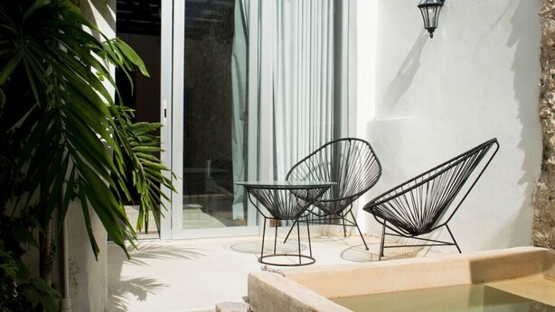 An outdoor seating area with two black wireframe chairs and a small table, a concrete pool, and a potted plant. - Casa Tiago - Downtown & Romance by LAHOS (Mérida)