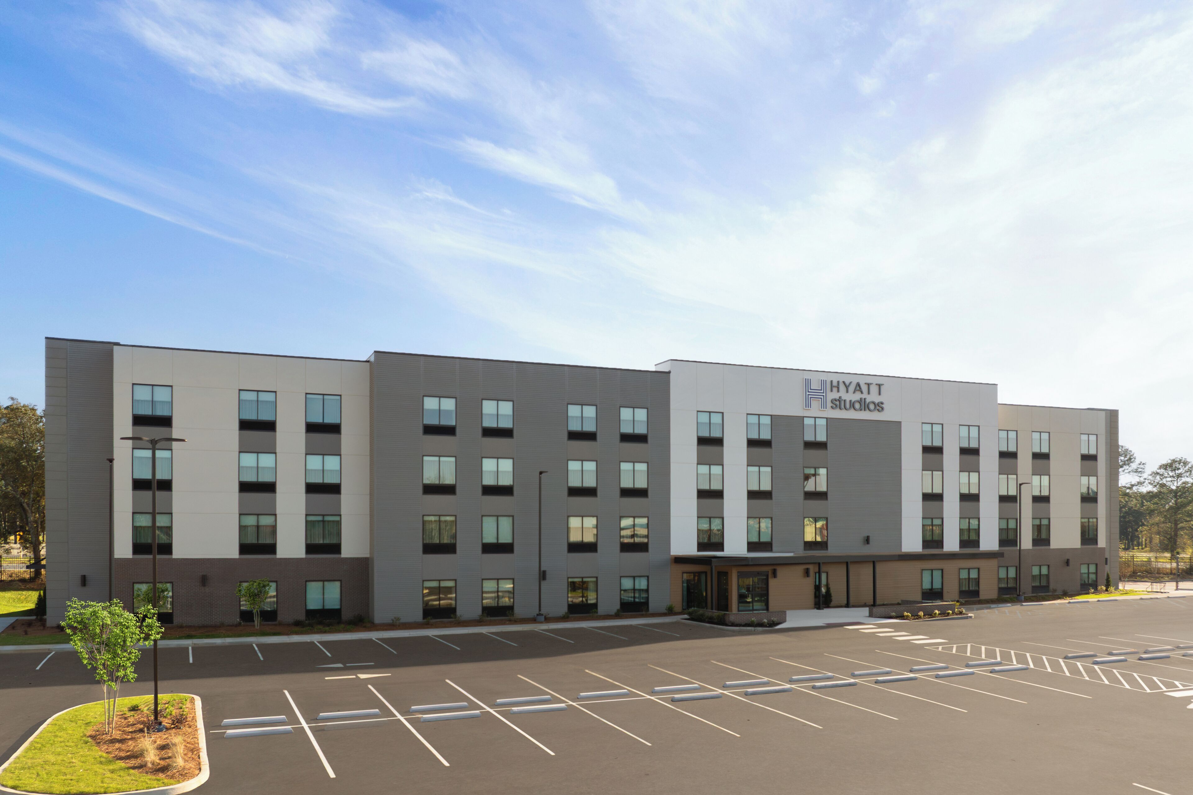 A modern hotel building with a flat roof, multiple windows, and a parking lot in front.