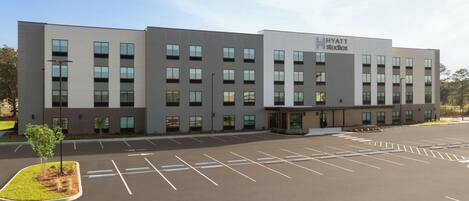 A modern hotel building with a flat roof, multiple windows, and a parking lot in front.
