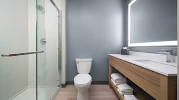 A modern bathroom with a glass shower enclosure, a white toilet, a wooden vanity with a mirror, and neatly folded towels.