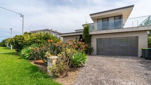A modern two-story house with a large garage, a balcony, and a well-maintained garden with tropical plants. - Clifftop Luxury With Pool ~ Ultimate outdoor experience with a private pool (Kiama)