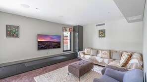 A modern living room with a flat-screen TV, a sofa set, a patterned rug, and a window with a view. - Clifftop Luxury With Pool ~ Ultimate outdoor experience with a private pool (Kiama)