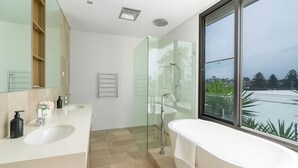 Een moderne badkamer met twee wastafels, een glazen douchecabine en een groot raam met uitzicht op de skyline.